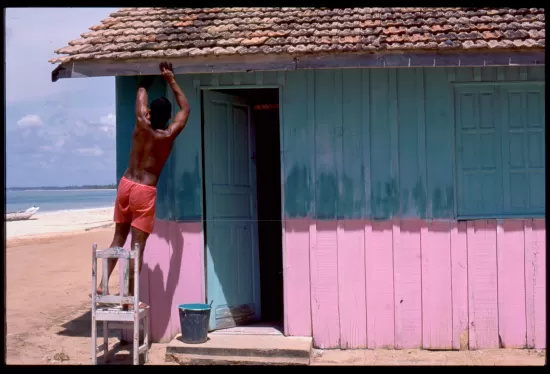 Man standing on ladder in front of teal and pink beach shack