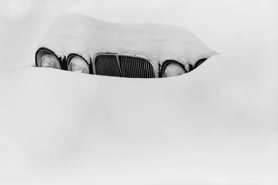 Black and white photo of an old car covered in snow
