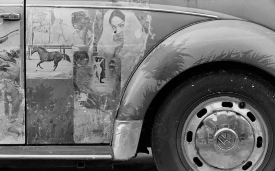 Black and white photo of an old Volkswagen Beetle decorated with magazine art